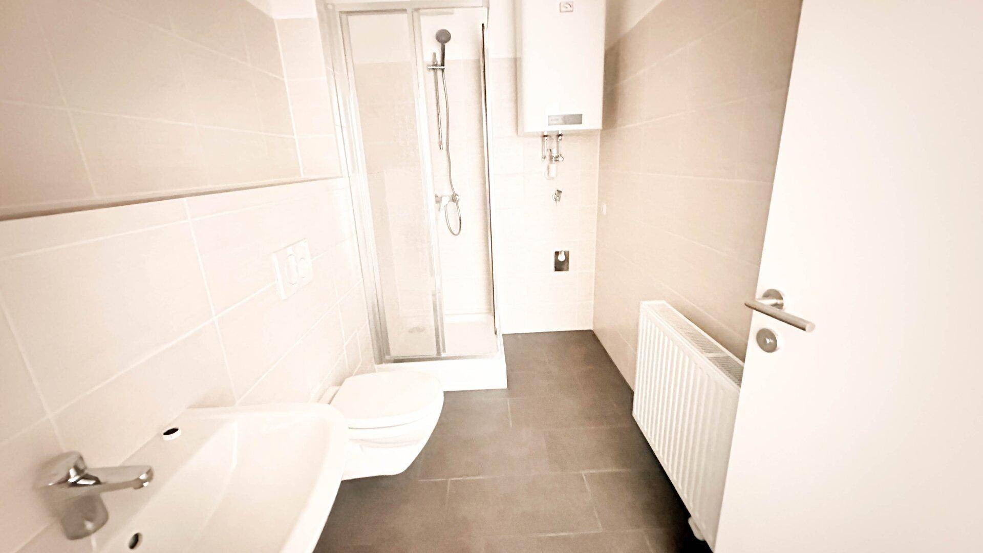 Modernes Badezimmer mit Duschkabine, WC, Waschbecken und Heizkörper in hellen Fliesen.