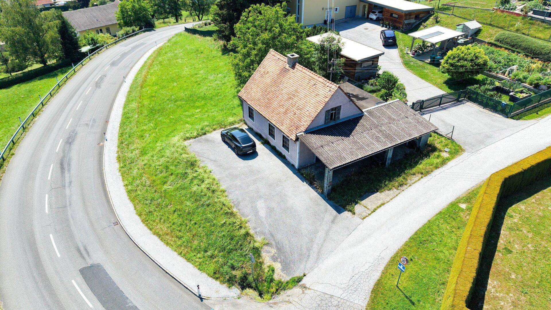 Luftaufnahme eines Hauses mit rotem Ziegeldach, angrenzendem Carport und einer Zufahrt an einer Kurve.
