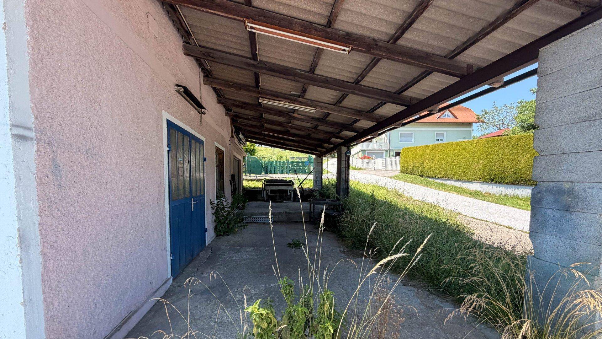 Überdachter Bereich mit Holzbalken und Betonboden, der als Carport oder Lagerfläche dient.