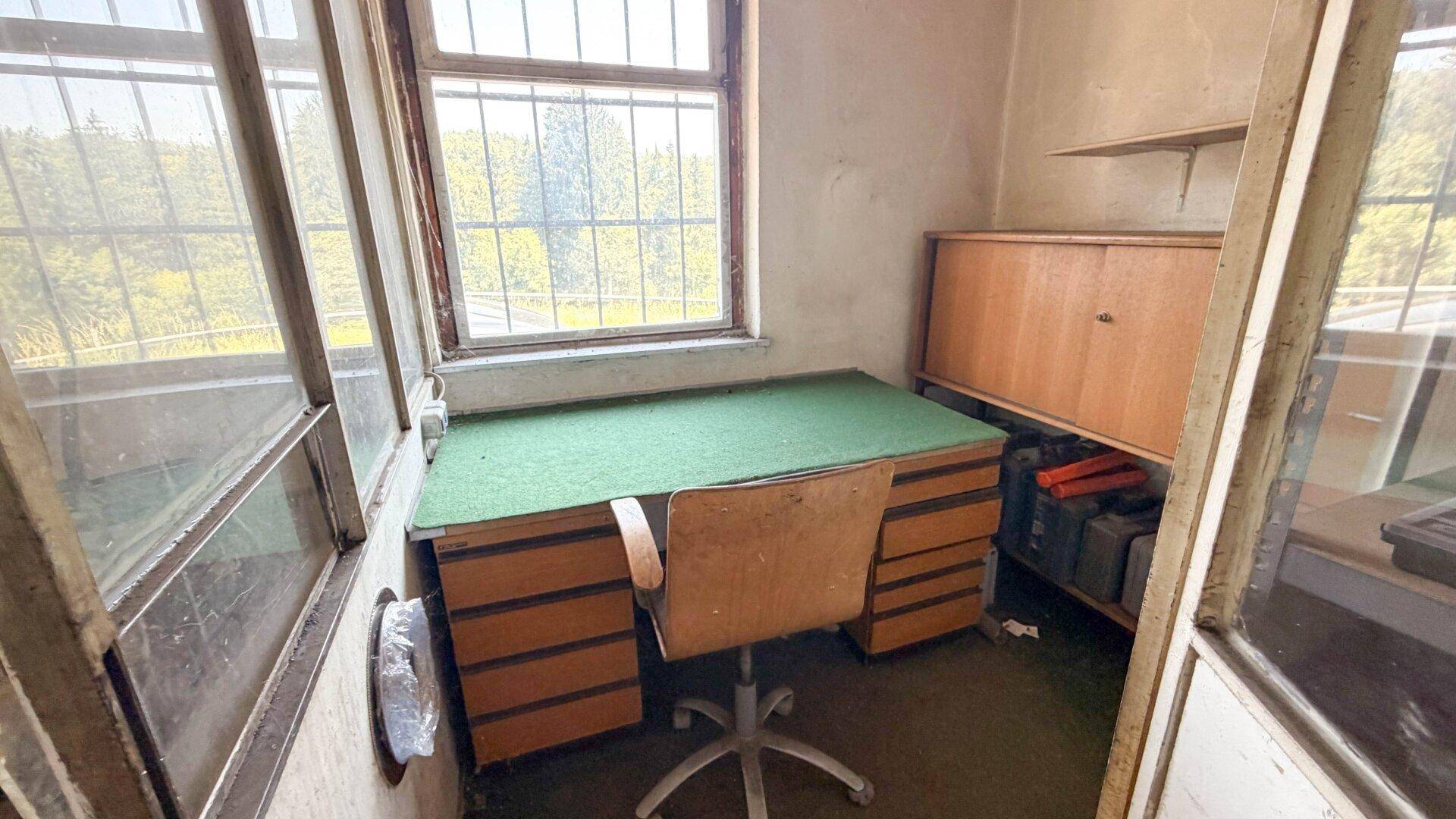 Kleines Büro mit Schreibtisch, Bürostuhl und Fenstern, die viel Tageslicht hereinlassen.