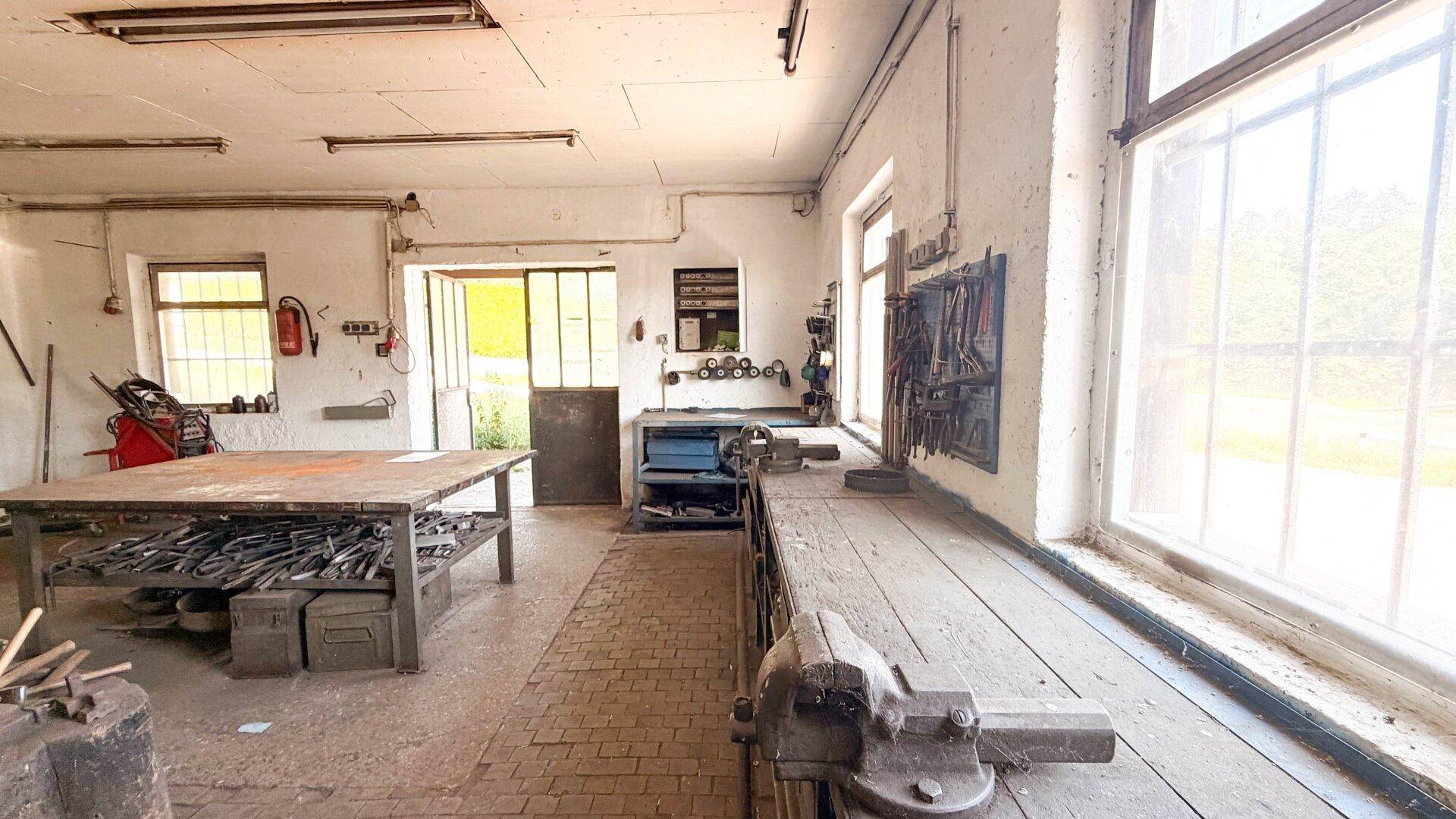 Helle Werkstatt mit langer Werkbank, Werkzeugen an der Wand und großen Fenstern.