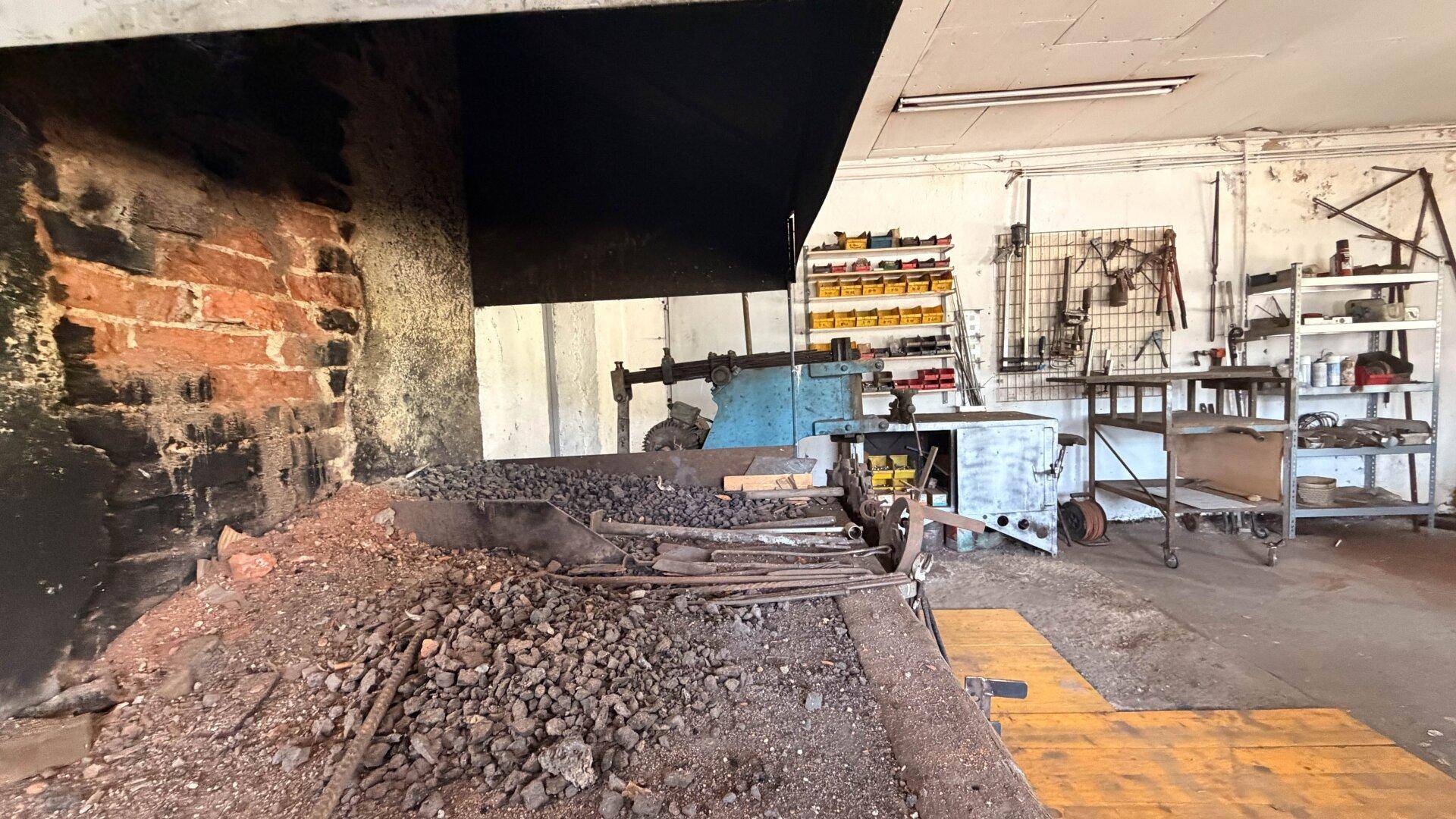 Nahaufnahme des gemauerten Schmiedeofens mit Kohle und Metallstücken in der Werkstatt.
