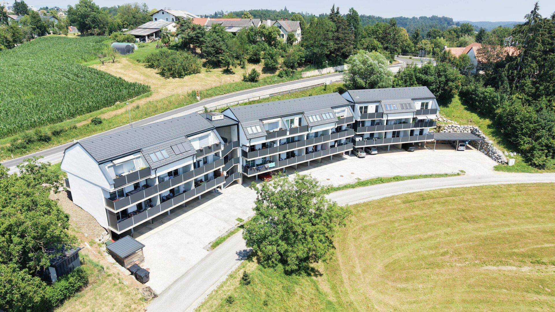 Luftaufnahme der modernen Wohnanlage, eingebettet in eine ländliche Umgebung mit Feldern und Zufahrtsstraße.