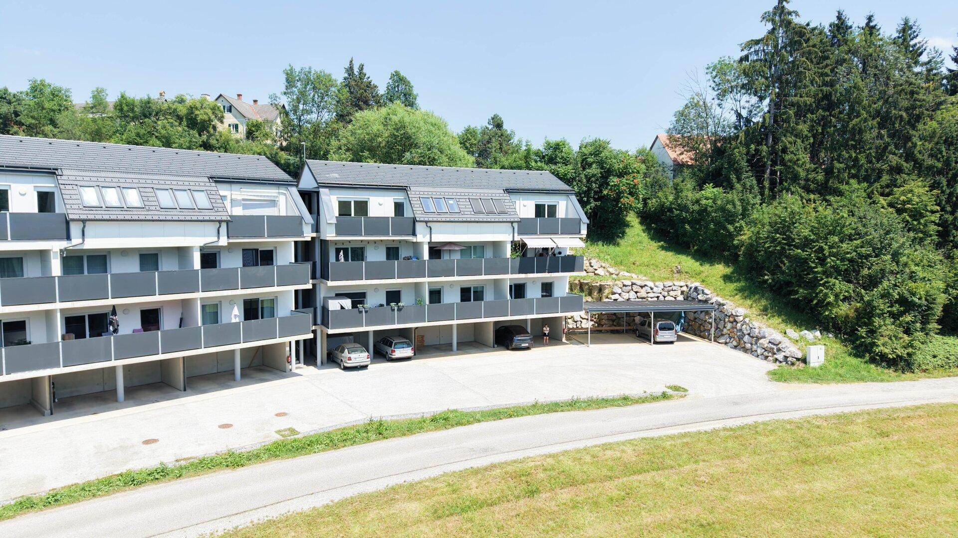 Ansicht der modernen Wohngebäude mit Balkonen und überdachten Parkplätzen, umgeben von Grünflächen.