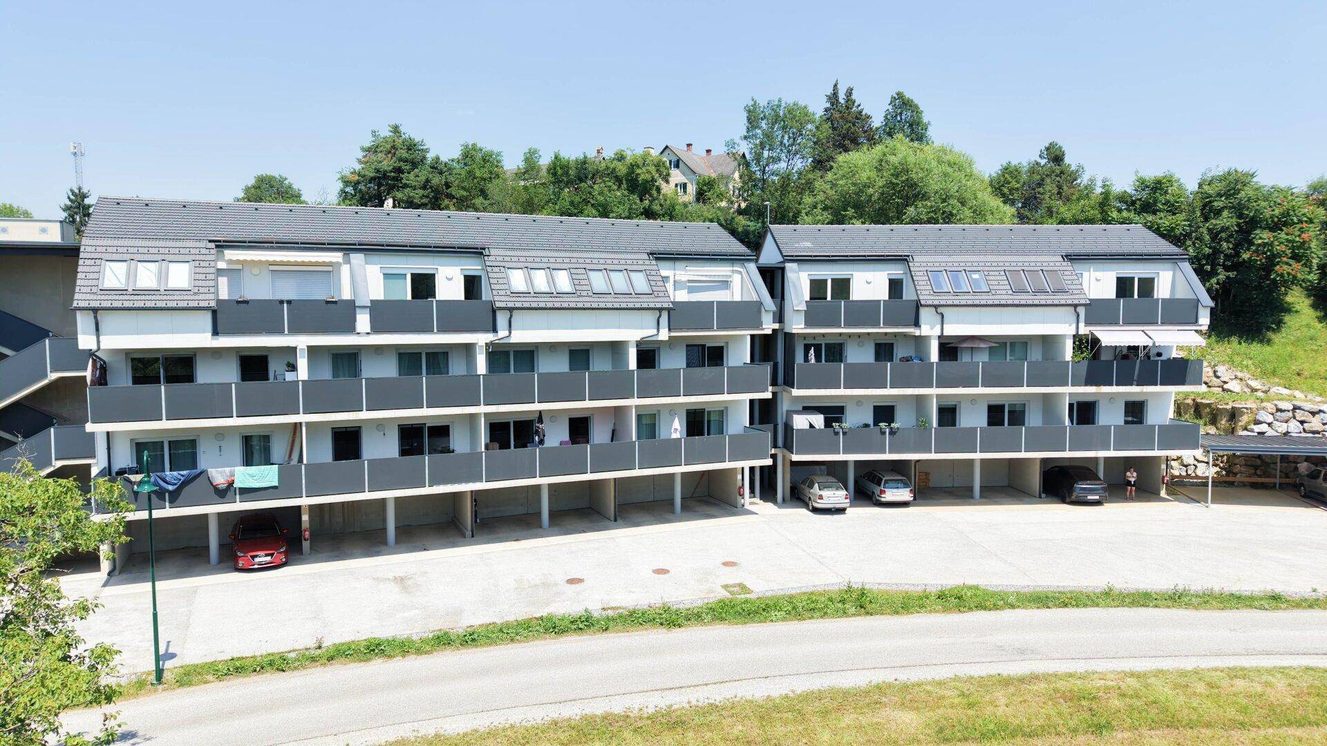 Fassade der modernen Wohnanlage mit mehreren Etagen, Balkonen und Parkmöglichkeiten im Freien.