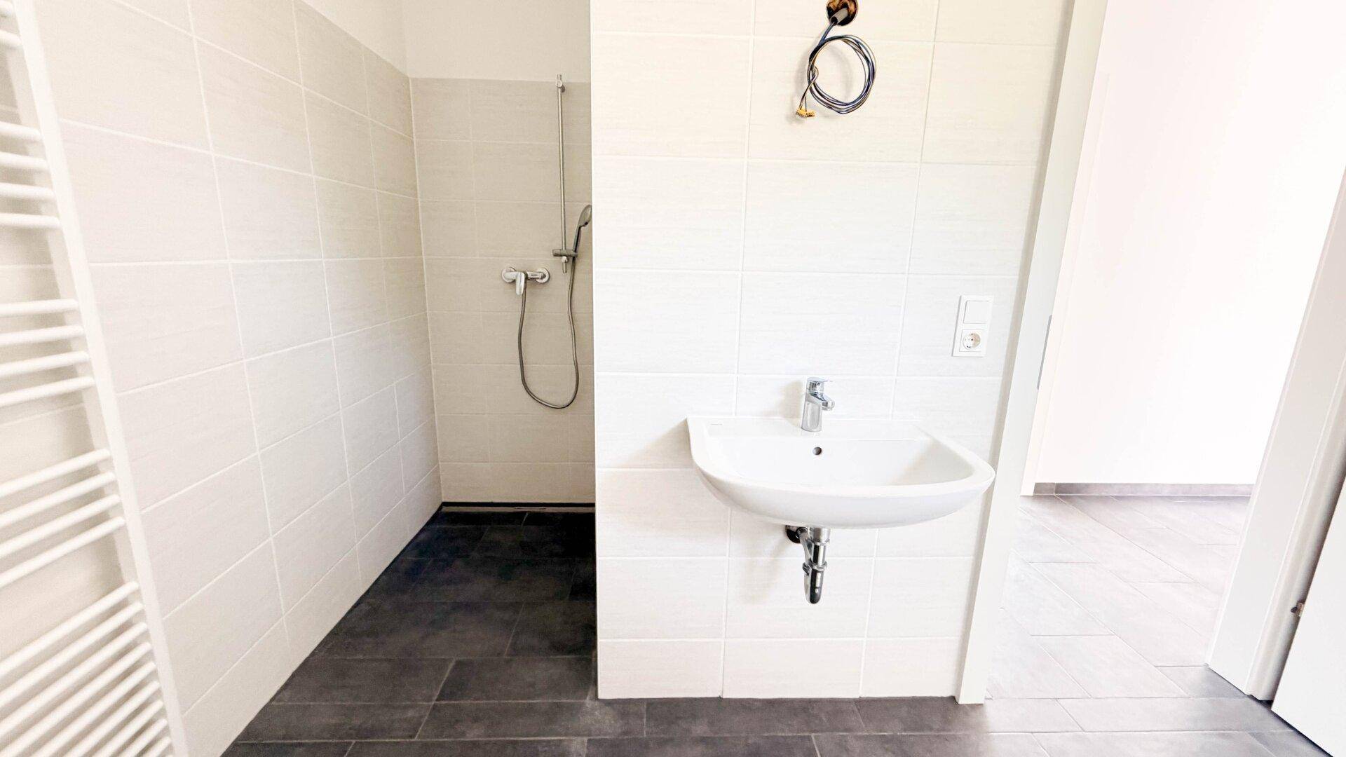 Badezimmer mit ebenerdiger Dusche, Waschbecken und hellen Wandfliesen.