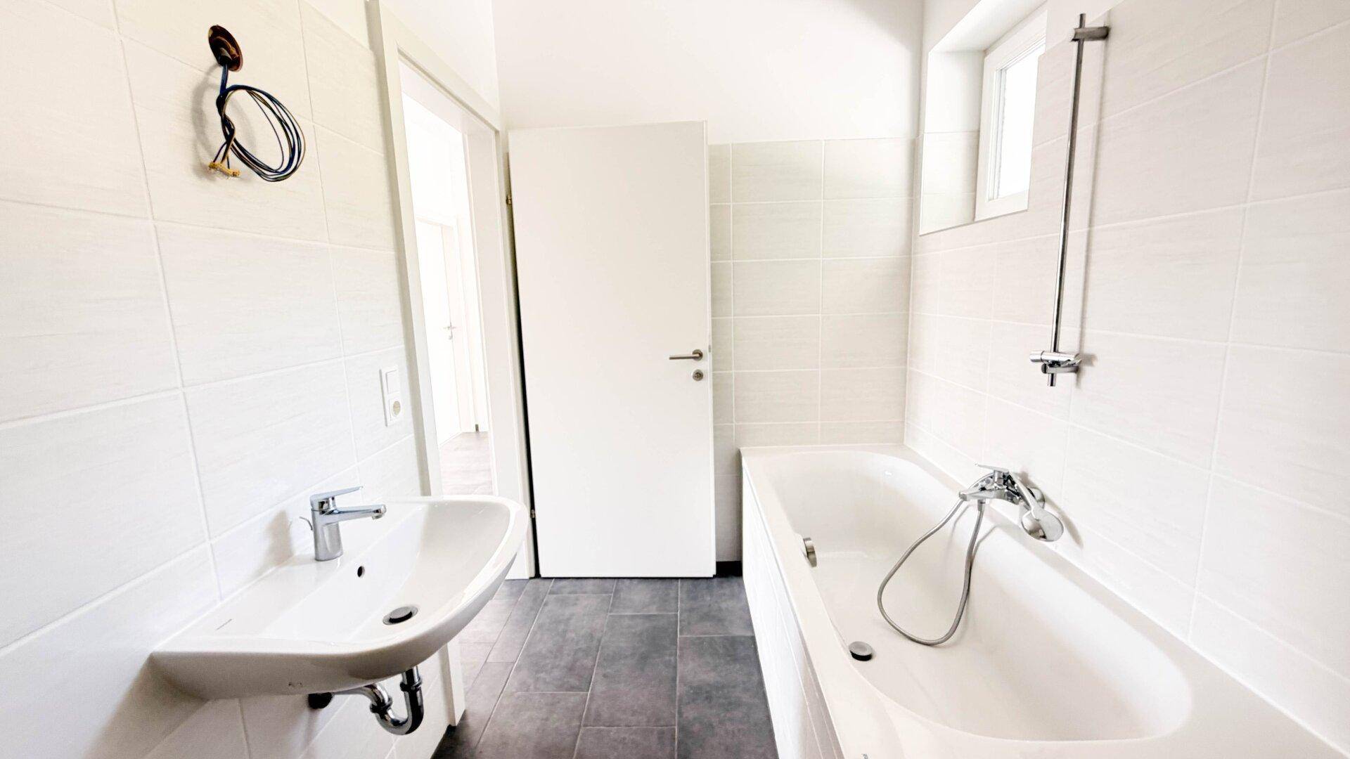 Modernes Badezimmer mit Badewanne, Waschbecken und hellen Fliesen.