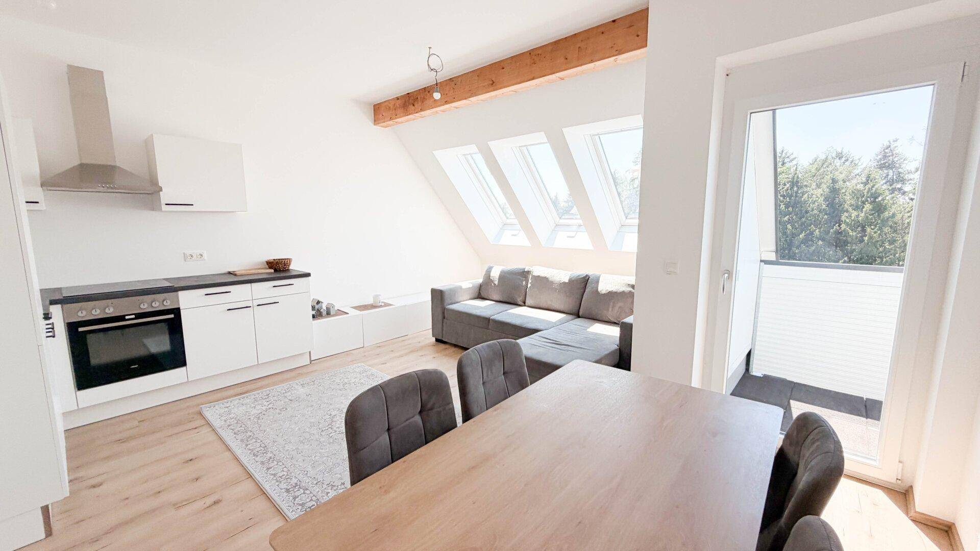 Lichtdurchfluteter Wohn-Essbereich mit Dachschrägen, offener Küche und Zugang zum Balkon.