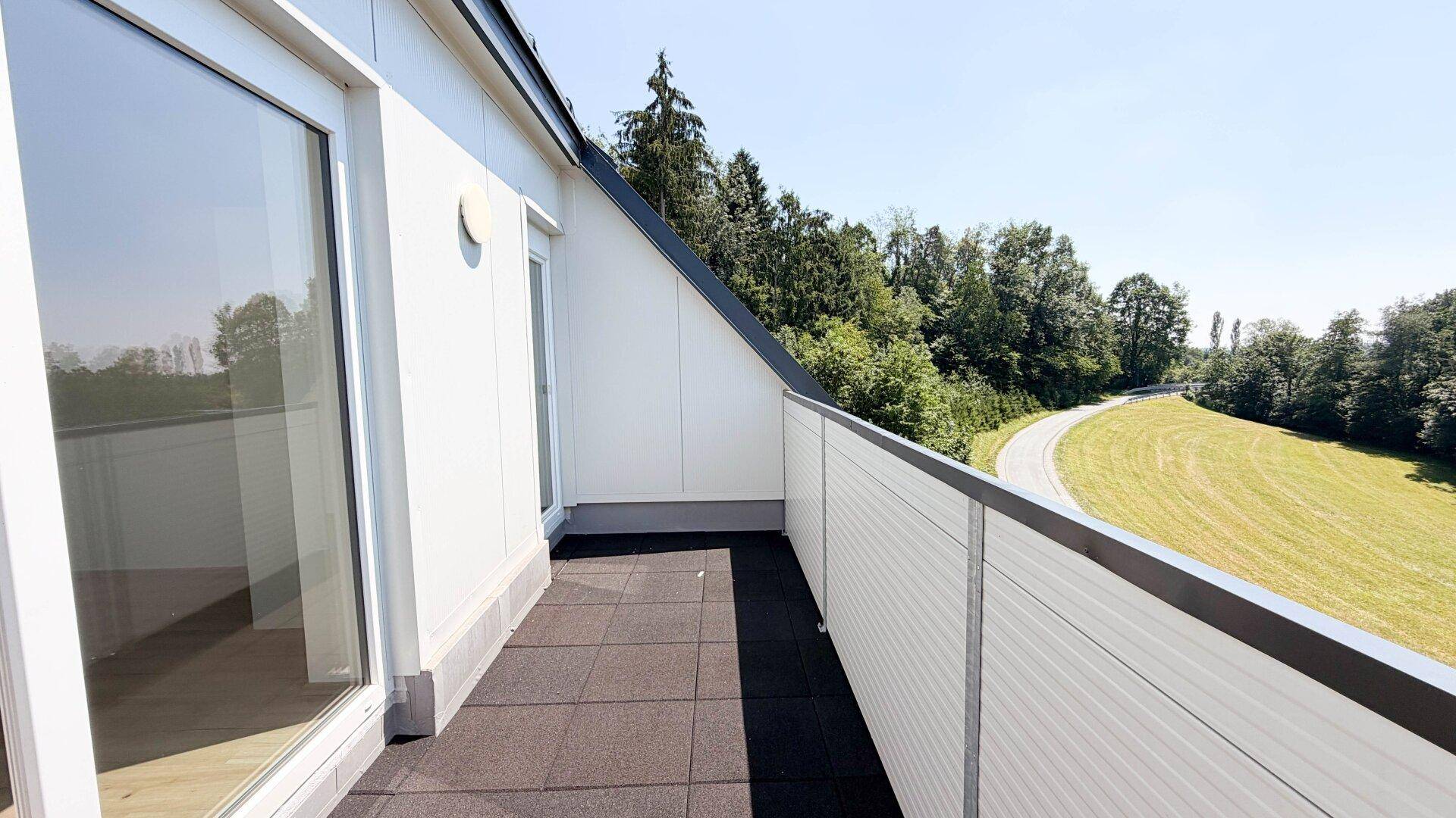 Langer Balkon mit Blick auf die grüne Umgebung und viel Sonnenlicht.