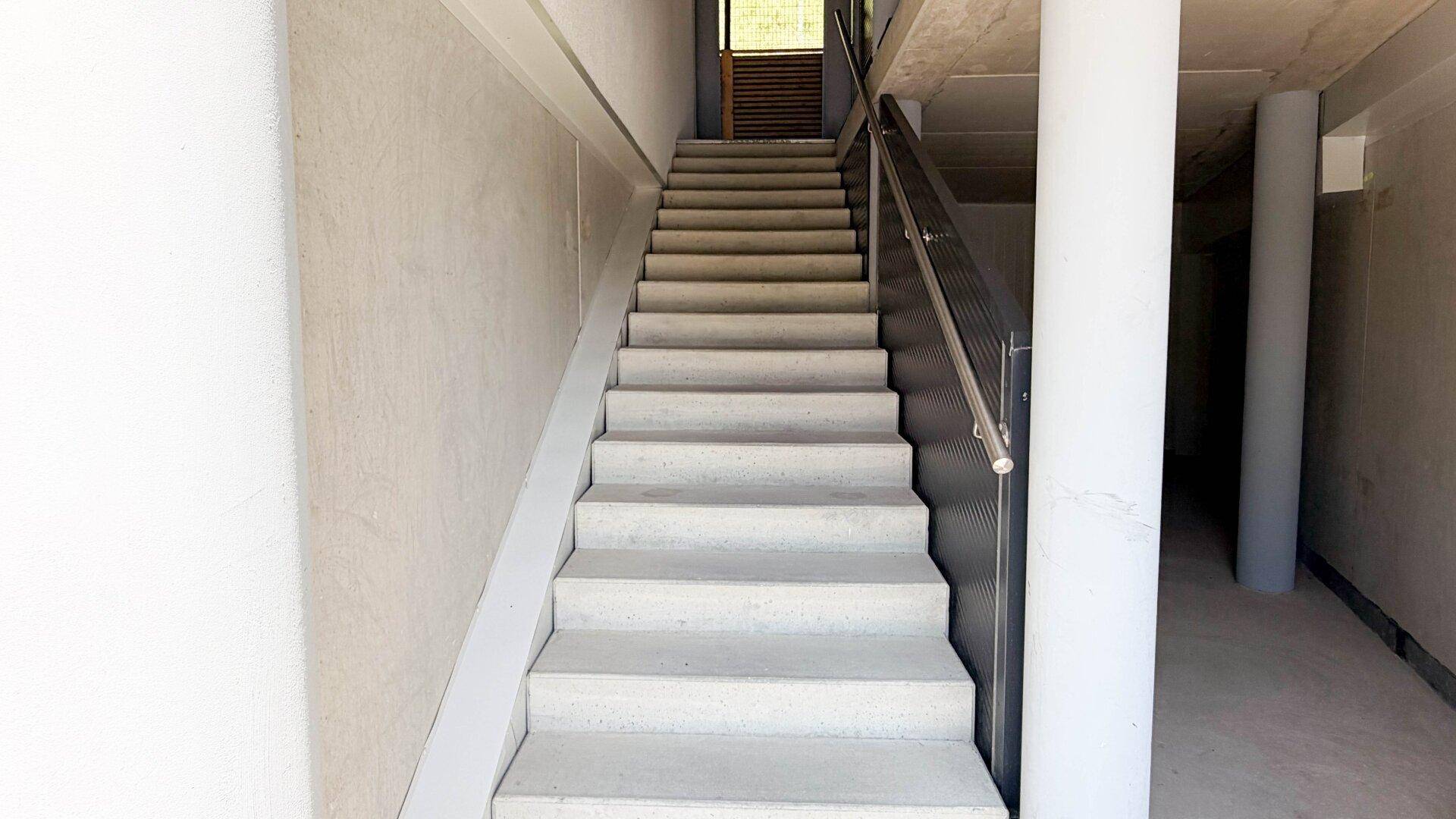 Geräumiges Treppenhaus mit Betonstufen und einem modernen Geländer, das zu den oberen Etagen führt.