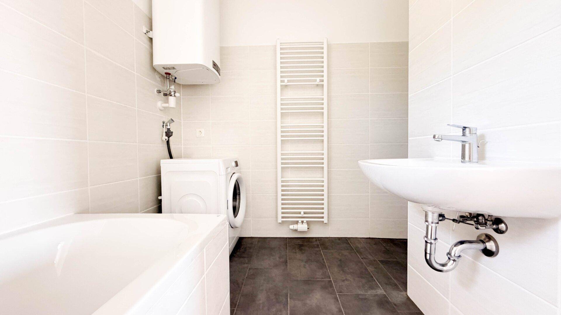 Badezimmer mit Badewanne, Waschmaschine und beheiztem Handtuchhalter.