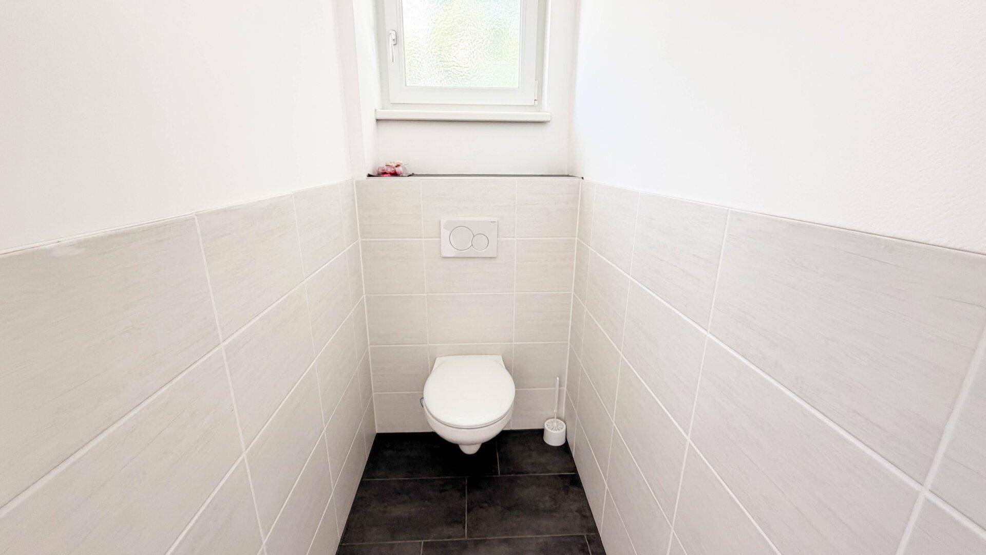 Separates Gäste-WC mit Wand-WC, Waschbecken und Fenster.