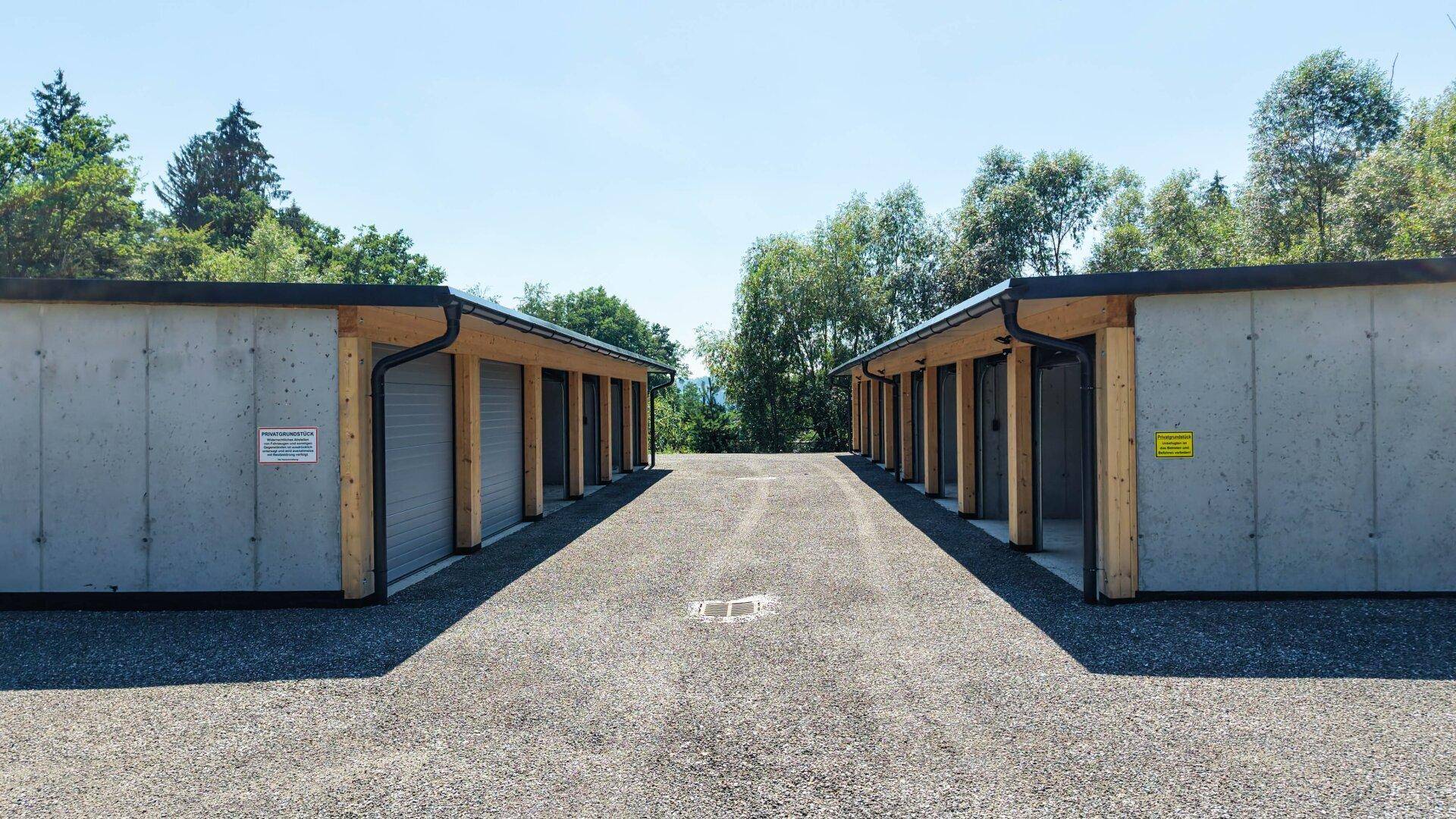 Zwei Reihen von Garagenboxen mit Betonwänden und Holzakzenten unter blauem Himmel.