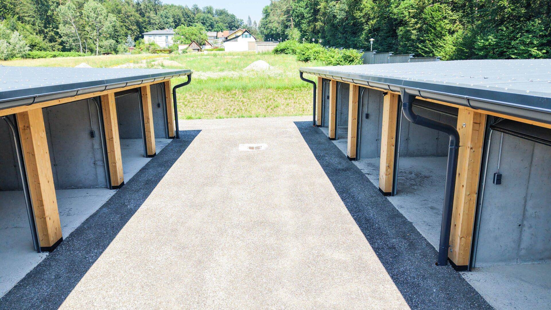 Blick auf zwei Reihen neuer Garagen- oder Lagereinheiten mit Betonfassaden und Holzelementen in ländlicher Umgebung.