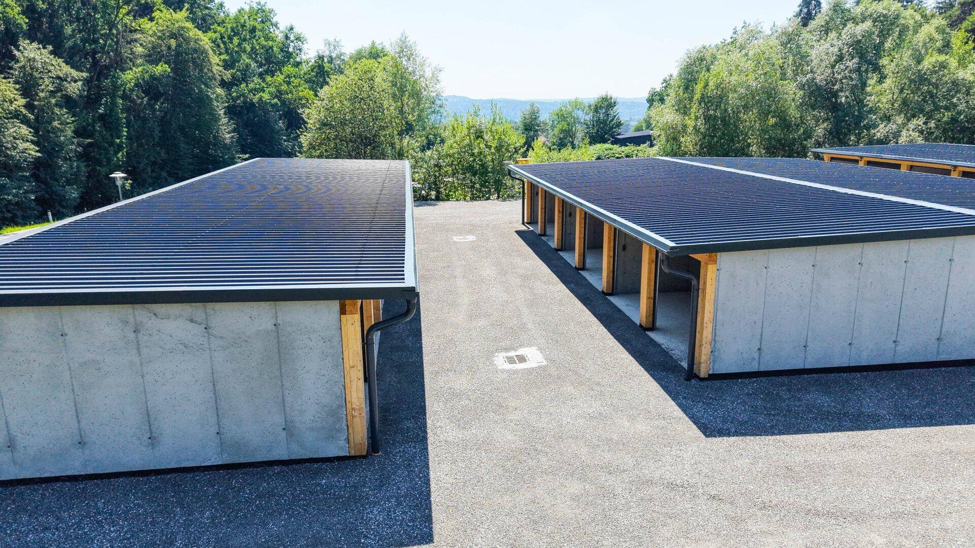 Zwei Blöcke moderner Garagen mit dunklen Dächern und Photovoltaik-Anlagen in ländlicher Umgebung.
