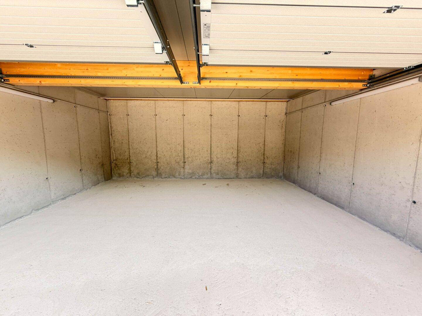 Leerer Innenraum einer modernen Garage mit Betonwänden, hellem Boden und sichtbarer Deckenkonstruktion.