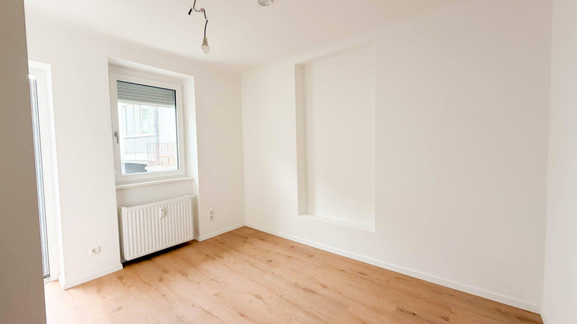 Heller Raum mit Holzfußboden, großem Fenster und Heizkörper, ideal als Wohn- oder Schlafzimmer.