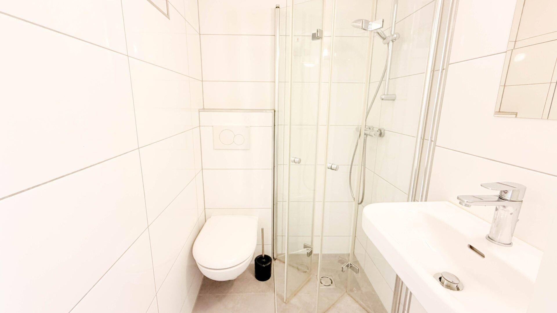 Modernes Badezimmer mit weißen Fliesen, Duschkabine, Toilette und Waschbecken.