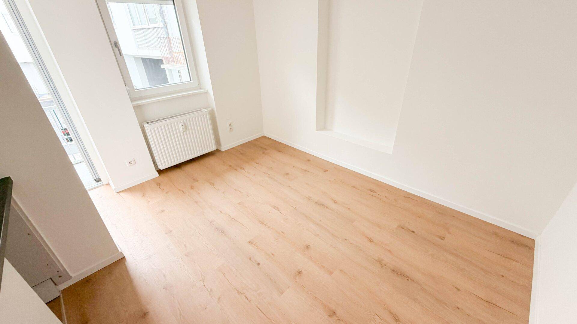 Geräumiger, heller Raum mit Holzfußboden, Fenster und Heizkörper, bereit zur individuellen Gestaltung.