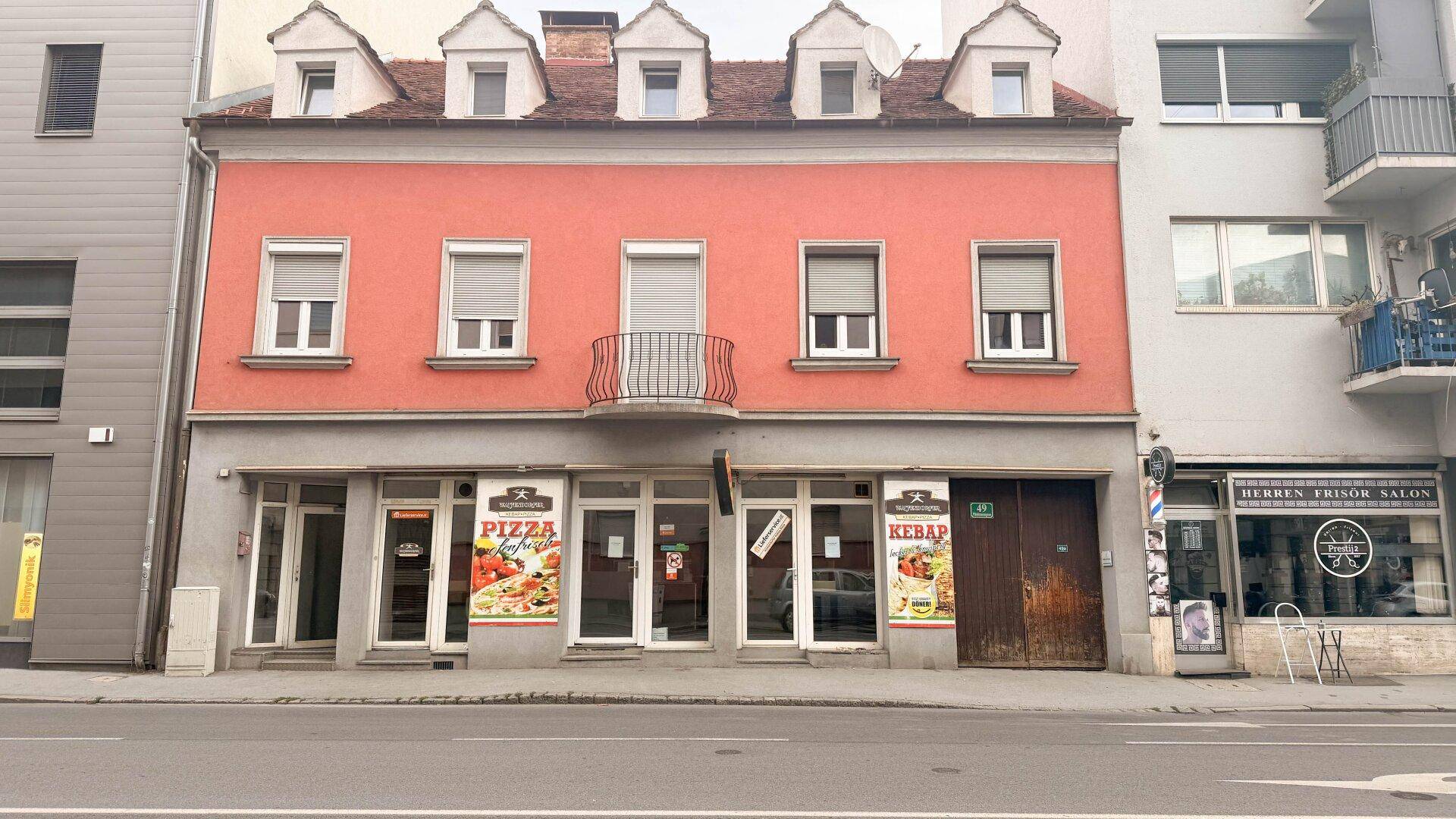 Fassade eines Mehrfamilienhauses mit Geschäften im Erdgeschoss und Wohnungen darüber.