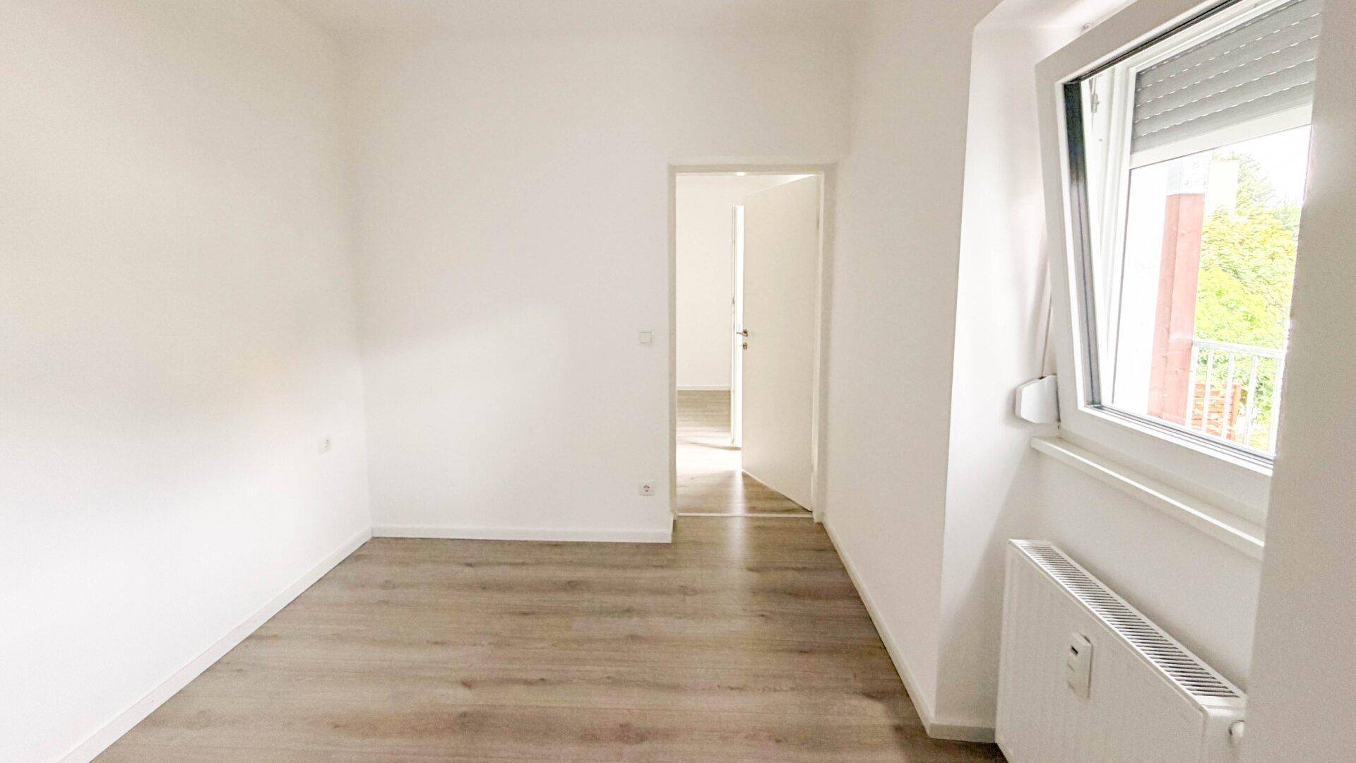 Geräumiges Schlafzimmer mit Laminatboden, weißen Wänden und natürlichem Lichteinfall.