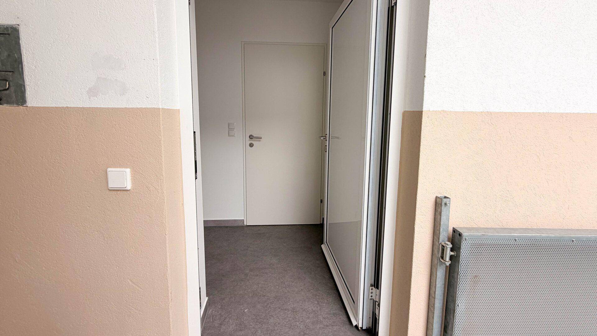 Eingangsbereich mit hellen Wänden und grauem Boden, führt zu den weiteren Räumen.