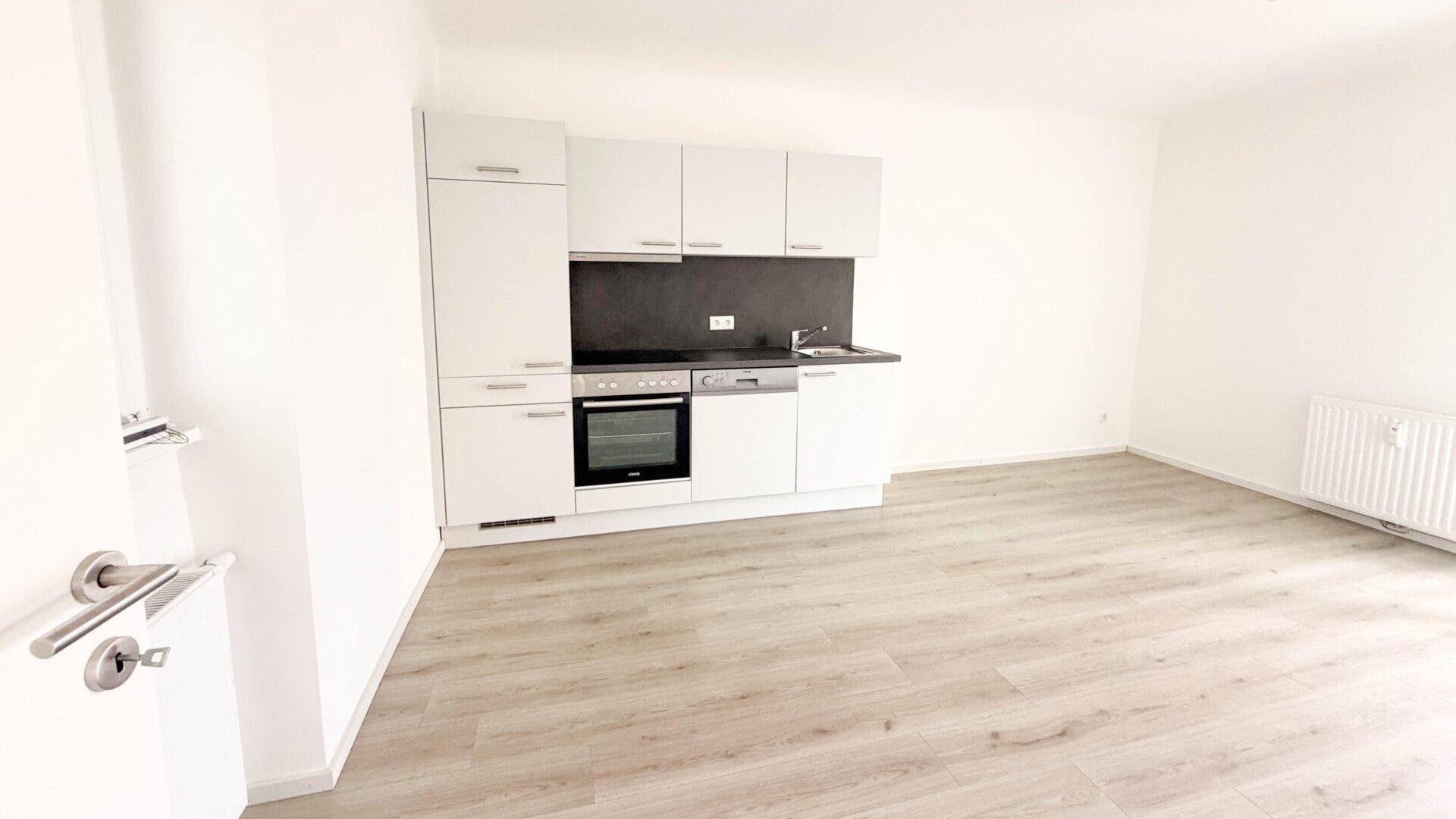 Moderner Wohnraum mit integrierter Küchenzeile, hellen Schränken und Laminatboden.
