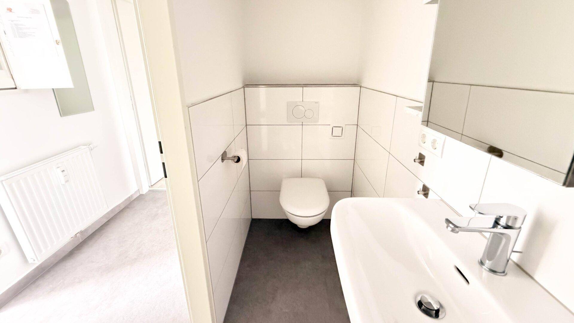 Kleines Gäste-WC mit modernen weißen Fliesen, Toilette und Handwaschbecken.