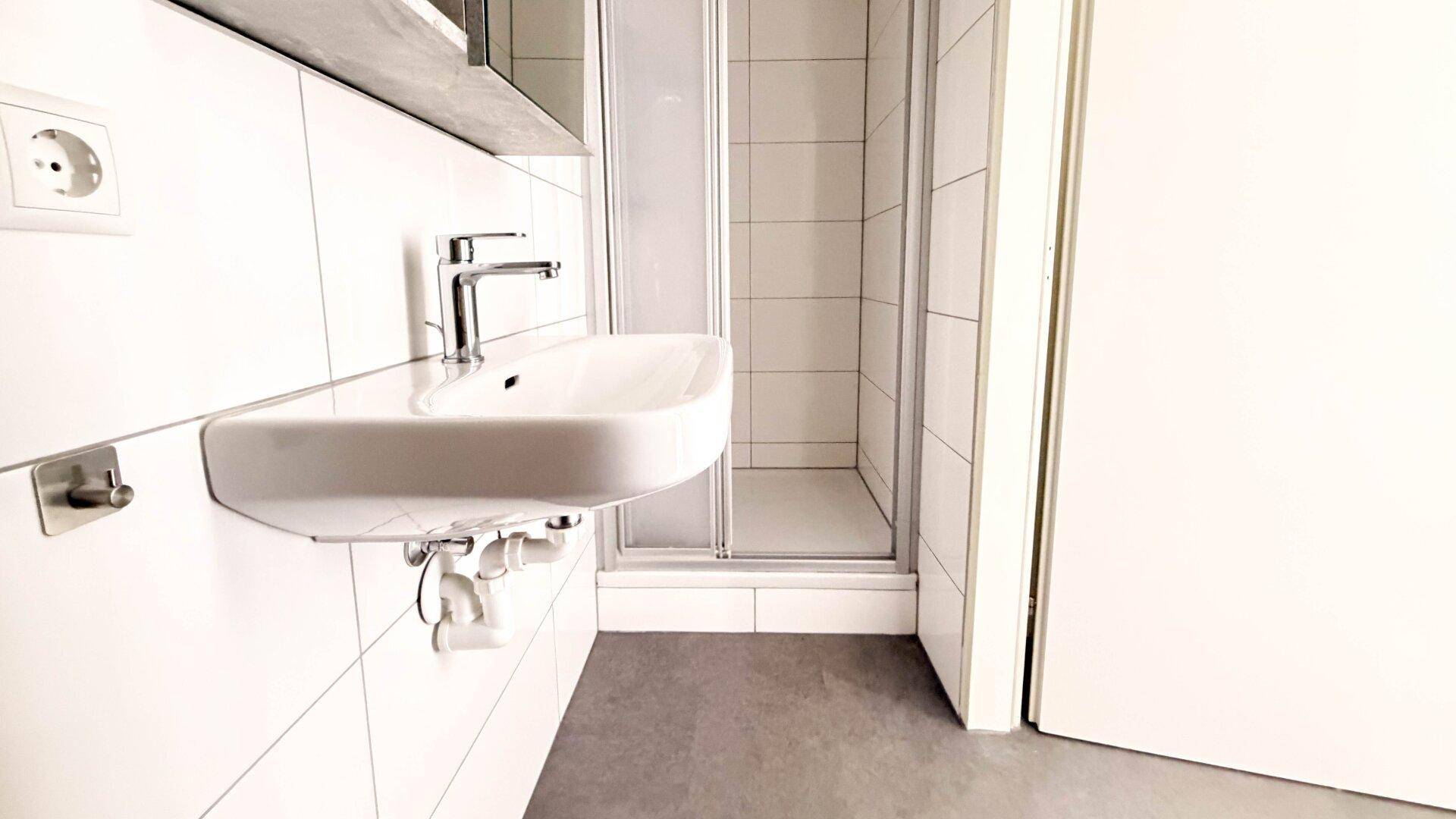 Modernes Badezimmer mit weißen Fliesen, Einzelwaschbecken und einer Duschkabine.