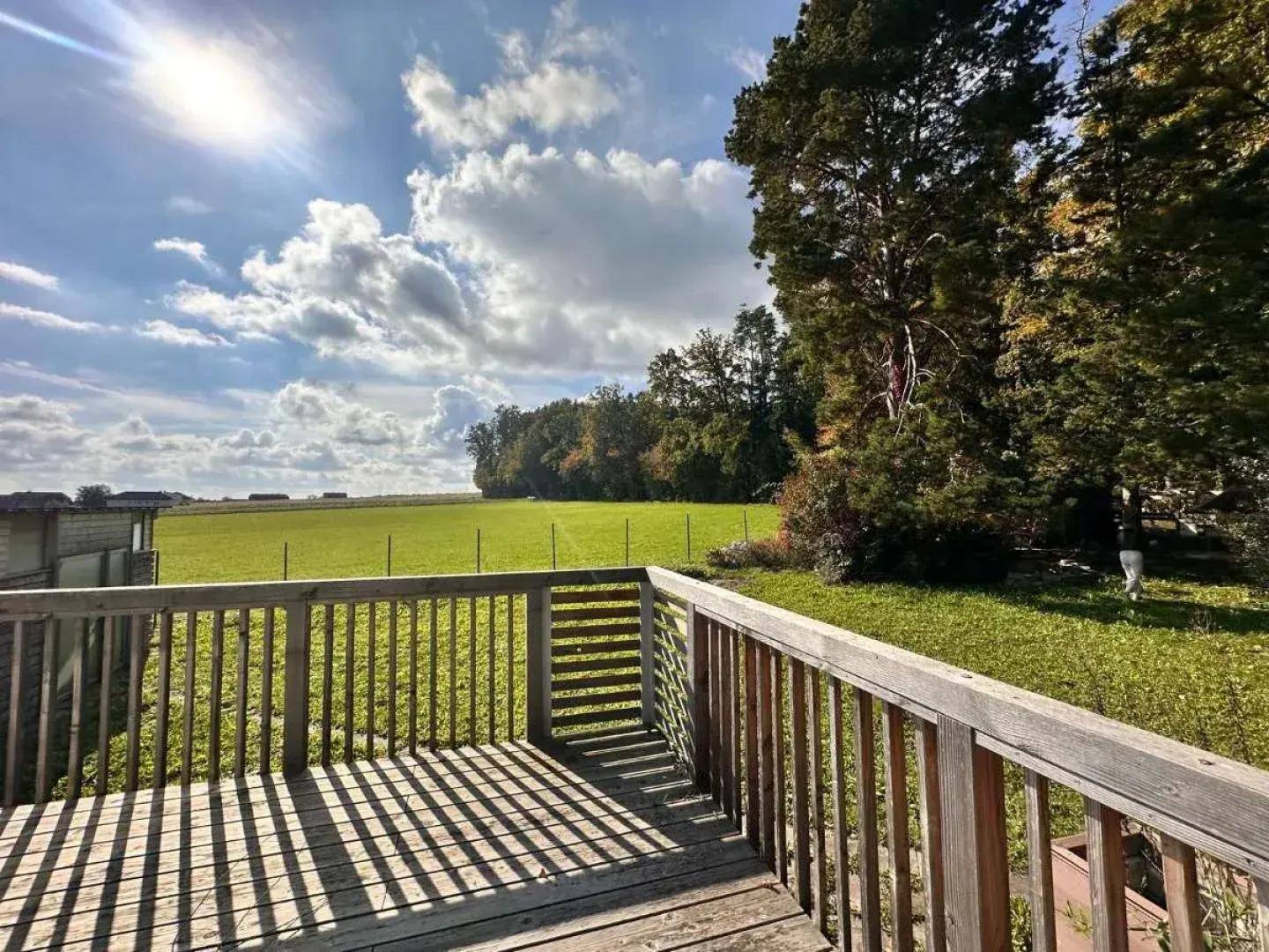 Sonniger Terrassenbereich mit Holzboden und weitem Blick über Felder und Landschaft.