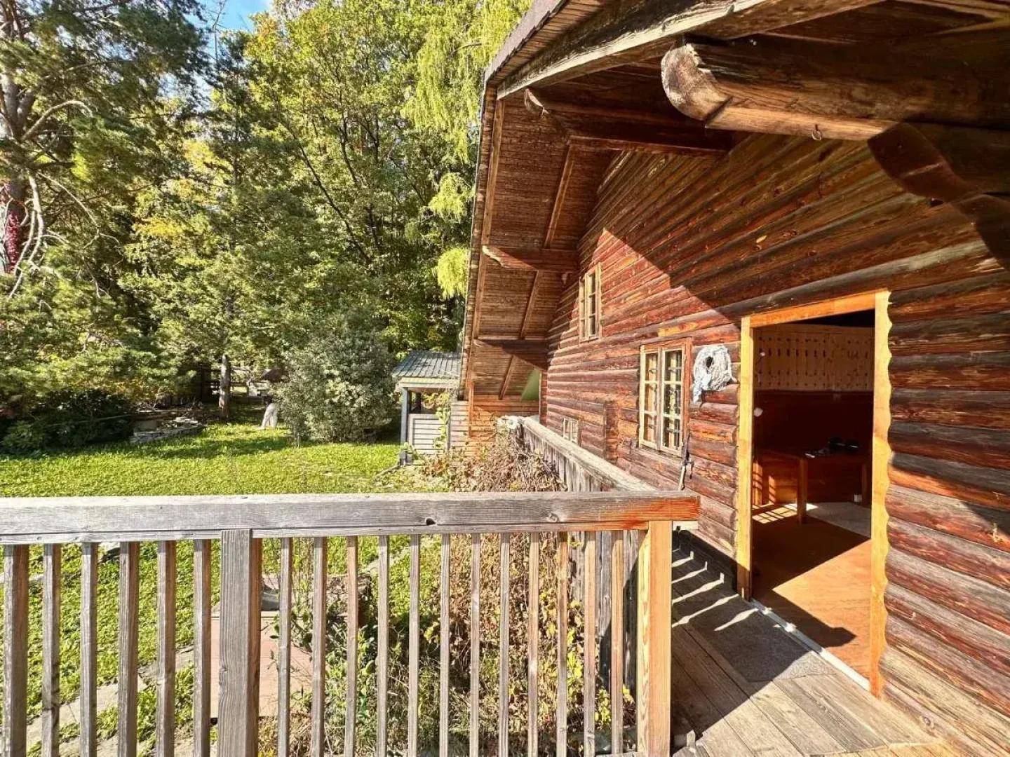 Holzterrasse am traditionellen Blockhaus mit Zugang zum Innenbereich und Blick ins Grüne.