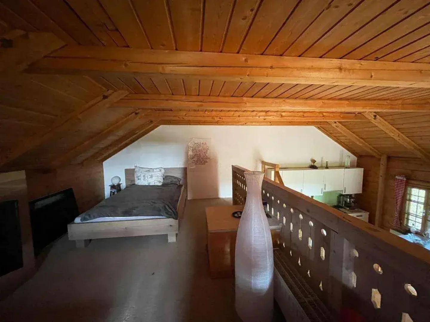 Gemütlicher Schlafbereich im Dachgeschoss mit Holzbalken und Blick auf den unteren Bereich.