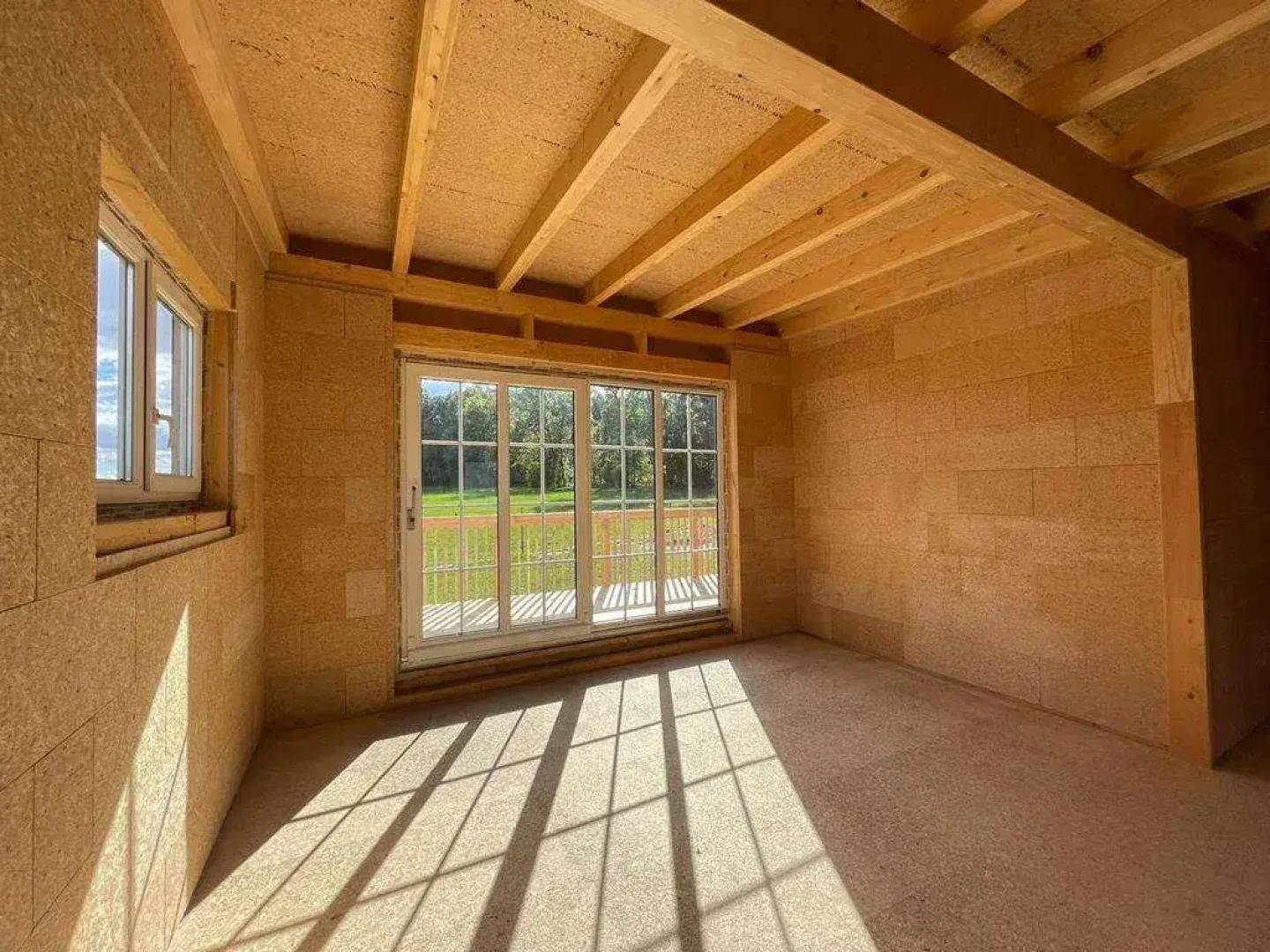 Geräumiger, unfertiger Raum mit Holzbalken und Schiebetüren zur Außenterrasse.
