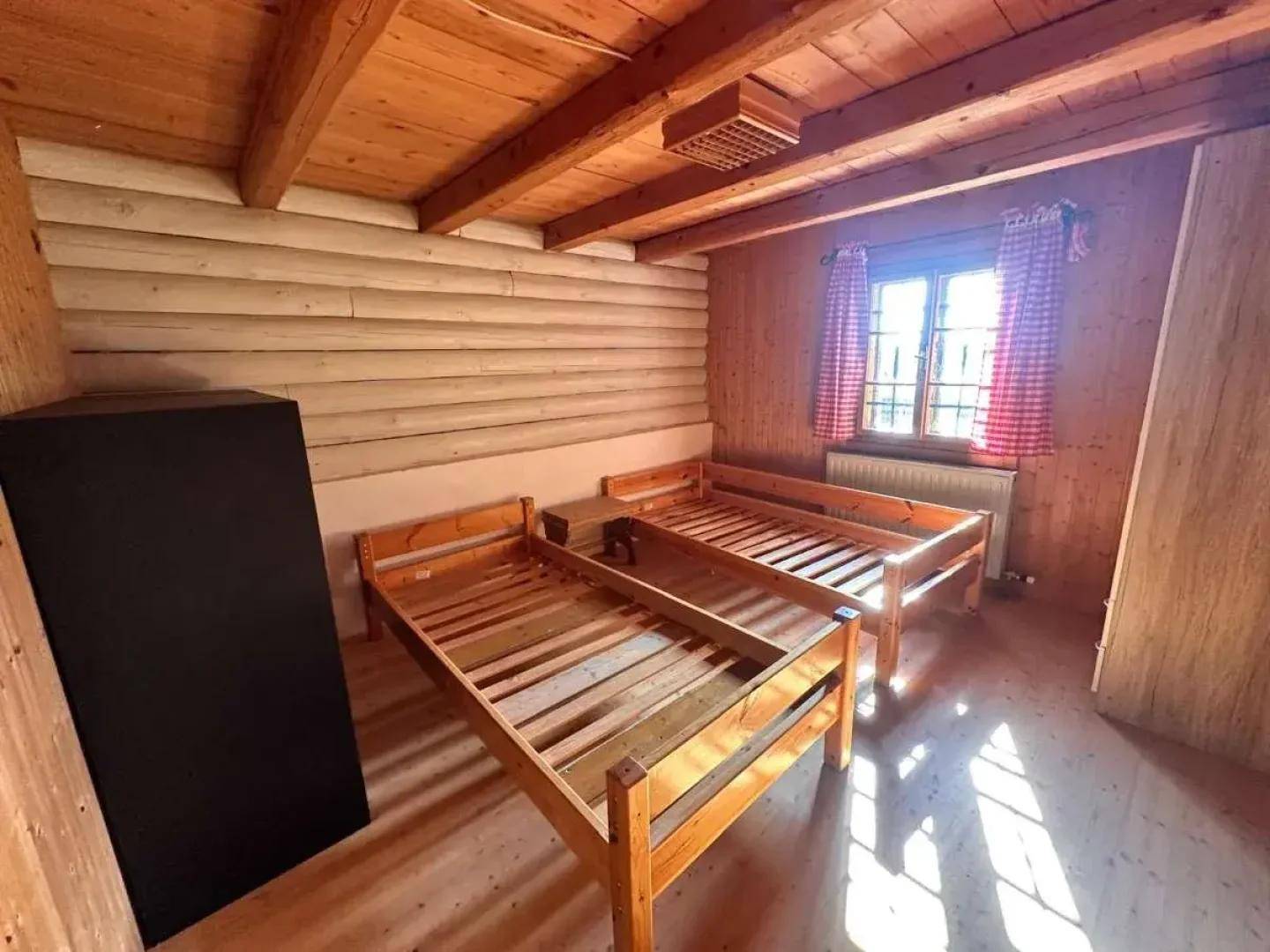Helles Schlafzimmer mit Holzwänden, Holzbalkendecke und zwei Einzelbetten.
