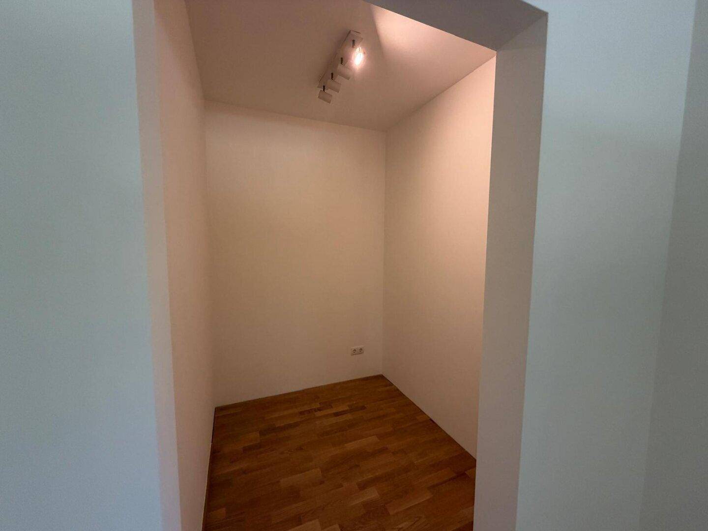 Kleiner, leerer Abstellraum mit Holzboden und weiß gestrichenen Wänden.