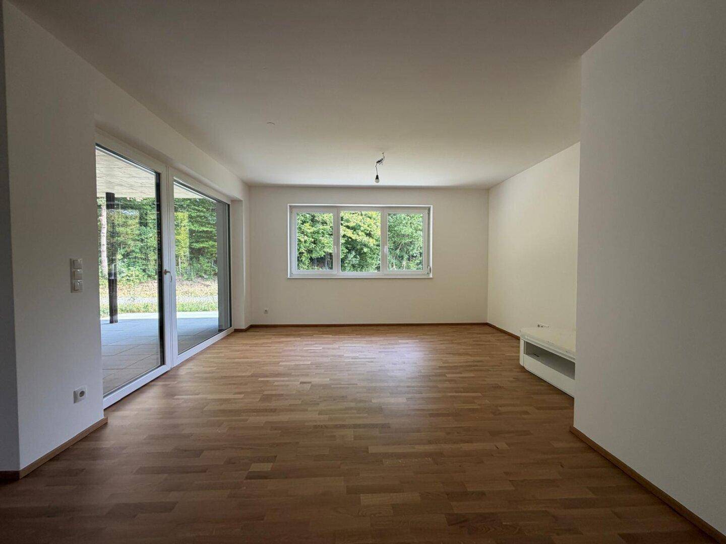 Helles Wohnzimmer mit Holzboden, großen Fenstern und Zugang zur Terrasse mit Grünblick.