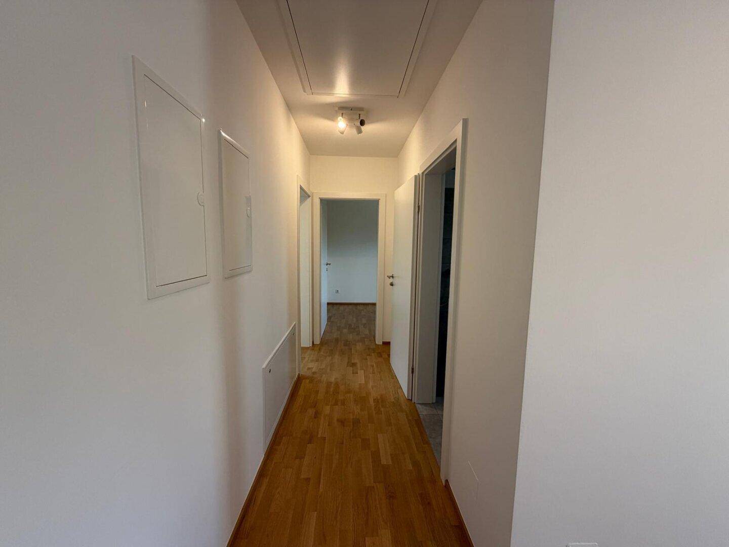 Heller Flur mit Holzboden, weißen Wänden und Zugang zu verschiedenen Räumen.