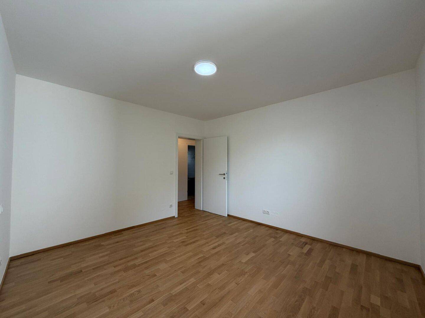 Helles Schlafzimmer mit Holzboden und weißen Wänden, bereit zur individuellen Gestaltung.