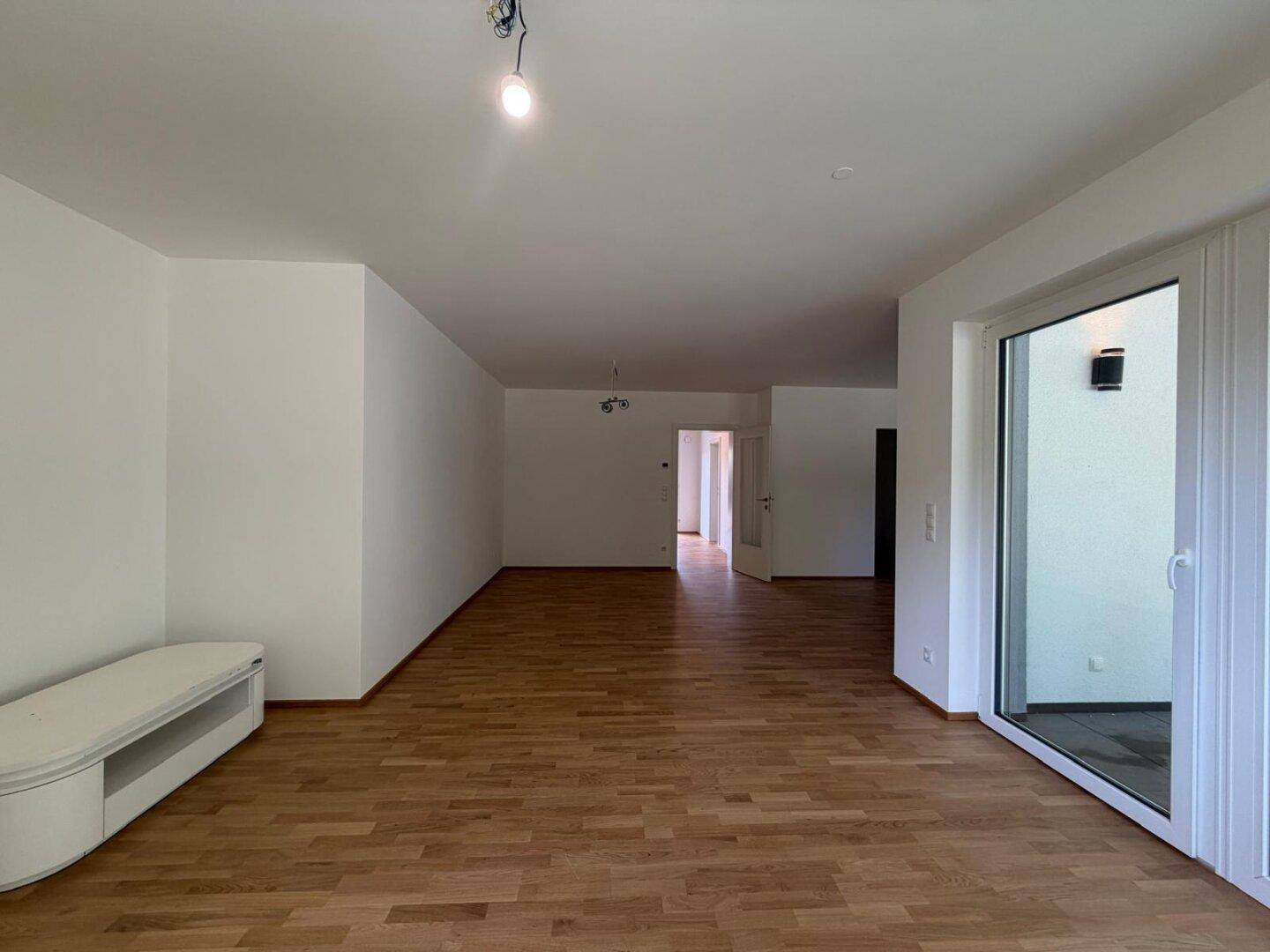 Geräumiger Wohnbereich mit Holzboden und weißen Wänden, offen zum Flur.