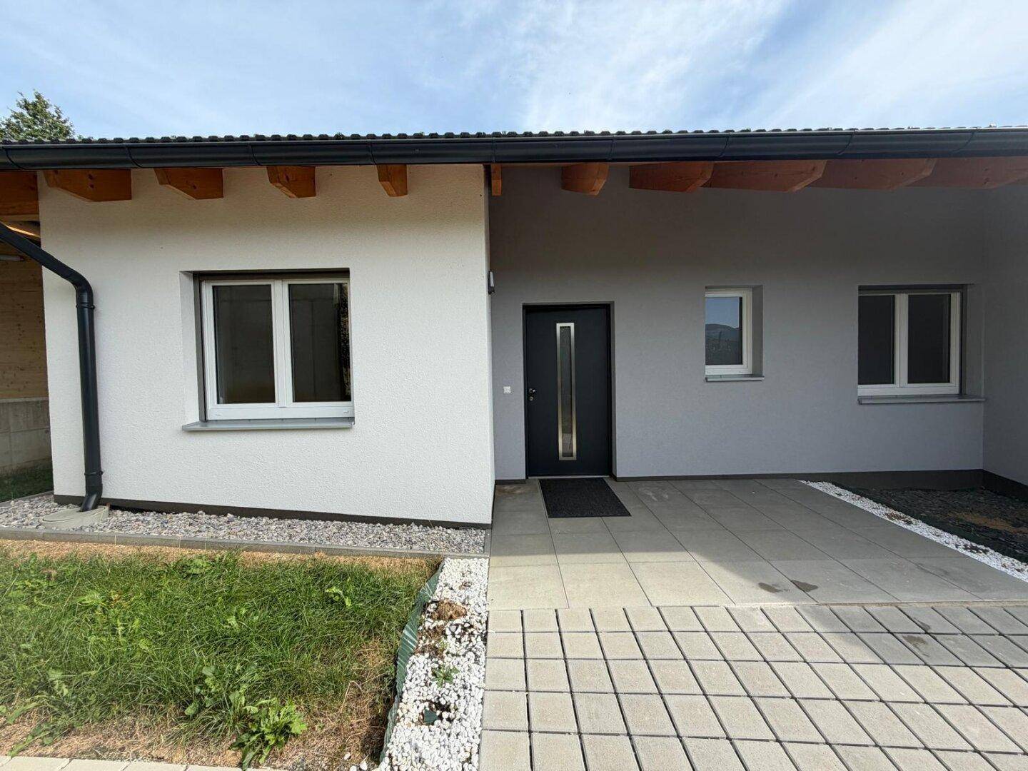 Eingangsbereich des modernen Hauses mit Haustür, Fenstern und gepflastertem Weg.