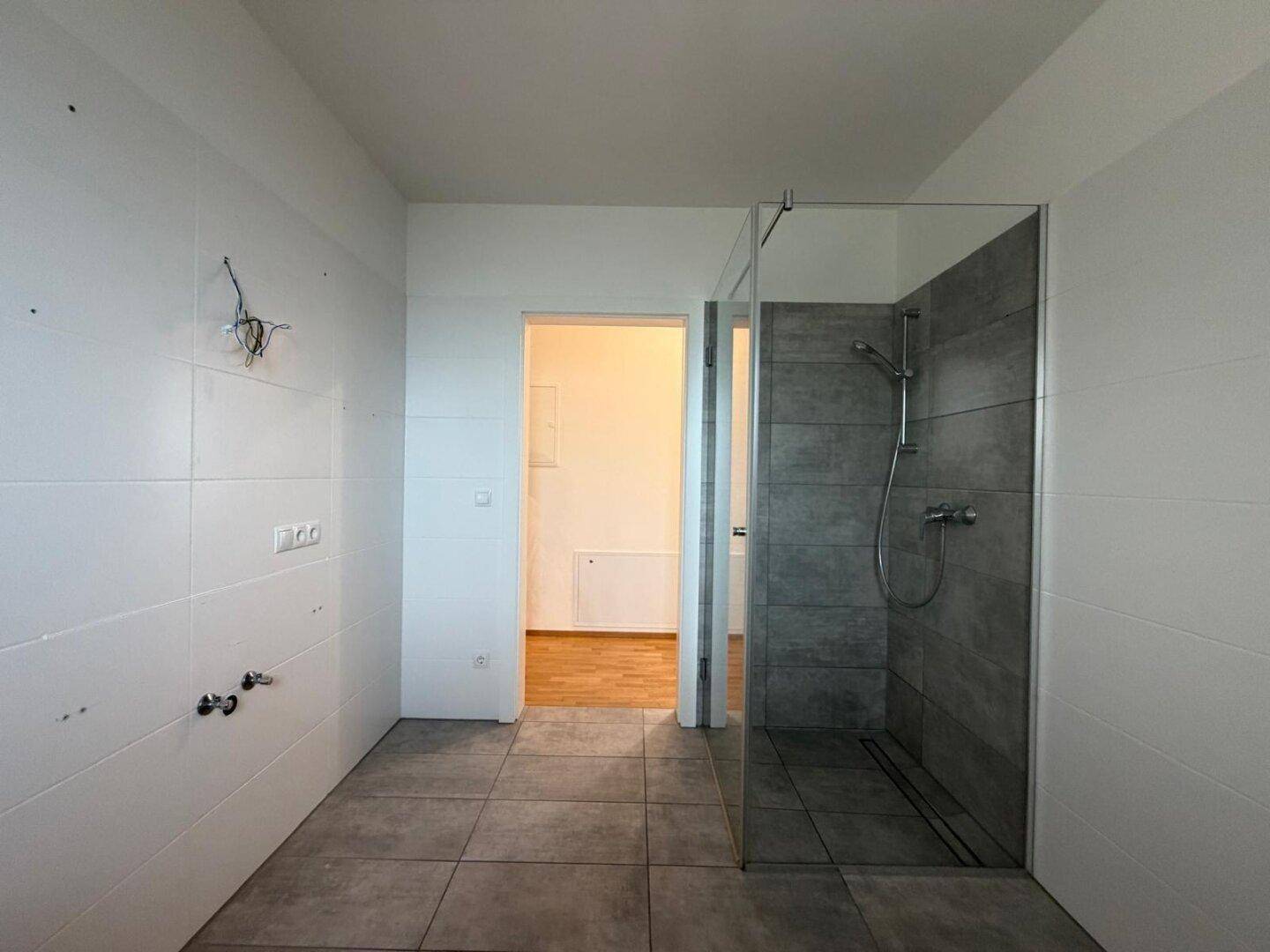 Modernes Badezimmer mit Fliesenboden, weißen Wänden und begehbarer Dusche mit Glasabtrennung.