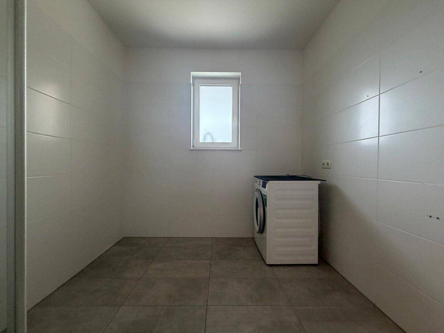 Praktischer Hauswirtschaftsraum mit Fliesenboden, Waschmaschine und Fenster.