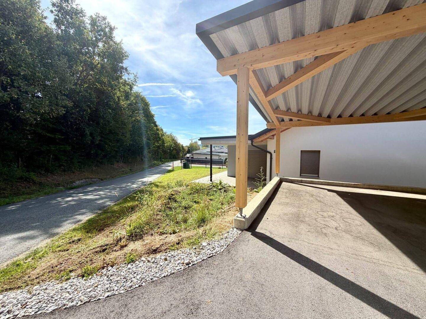 Überdachter Carportbereich mit Holzbalken und Blick auf die Zufahrtsstraße und Bäume.