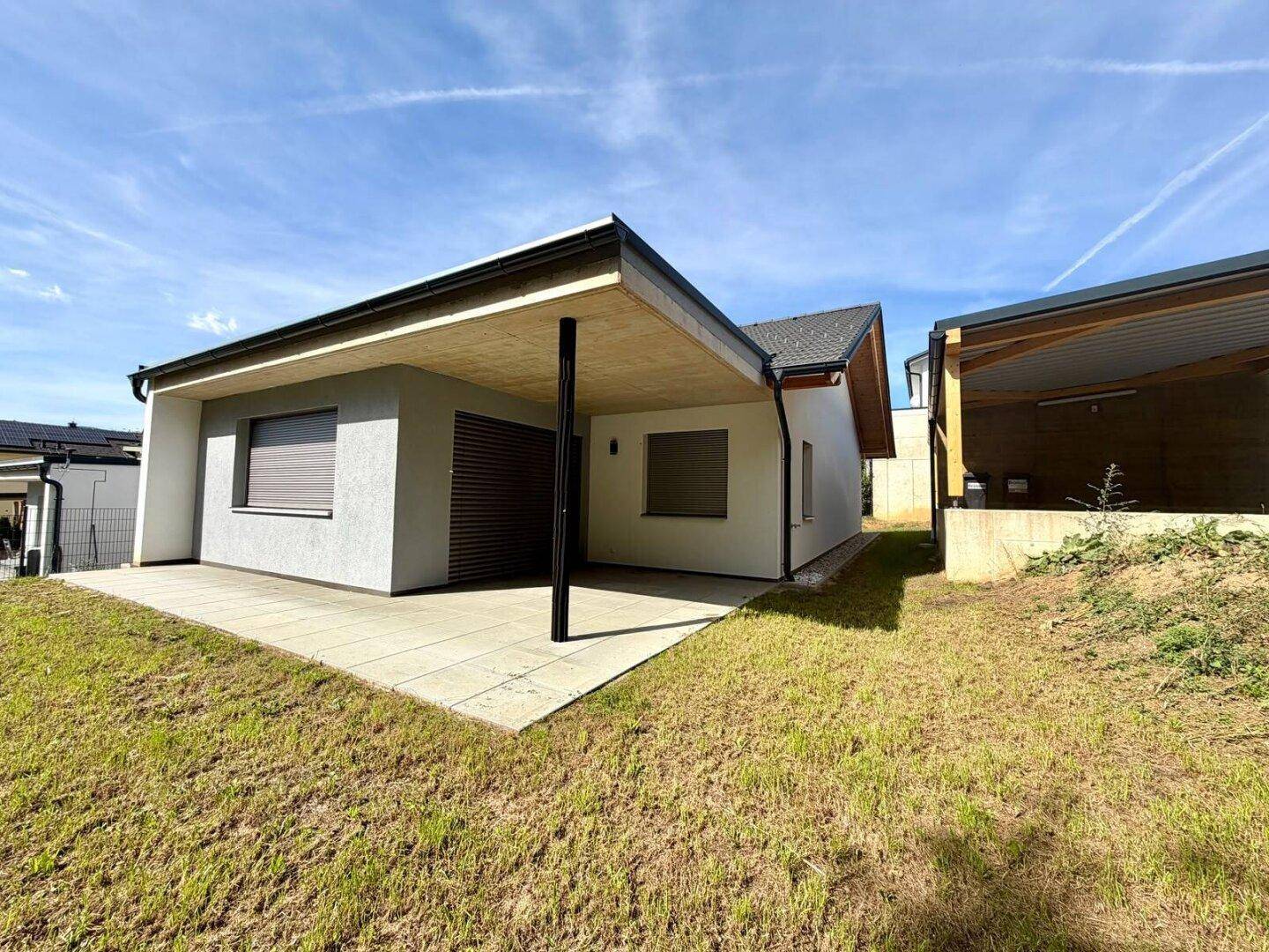 Moderne Terrasse mit Überdachung und angrenzender Rasenfläche am Haus.