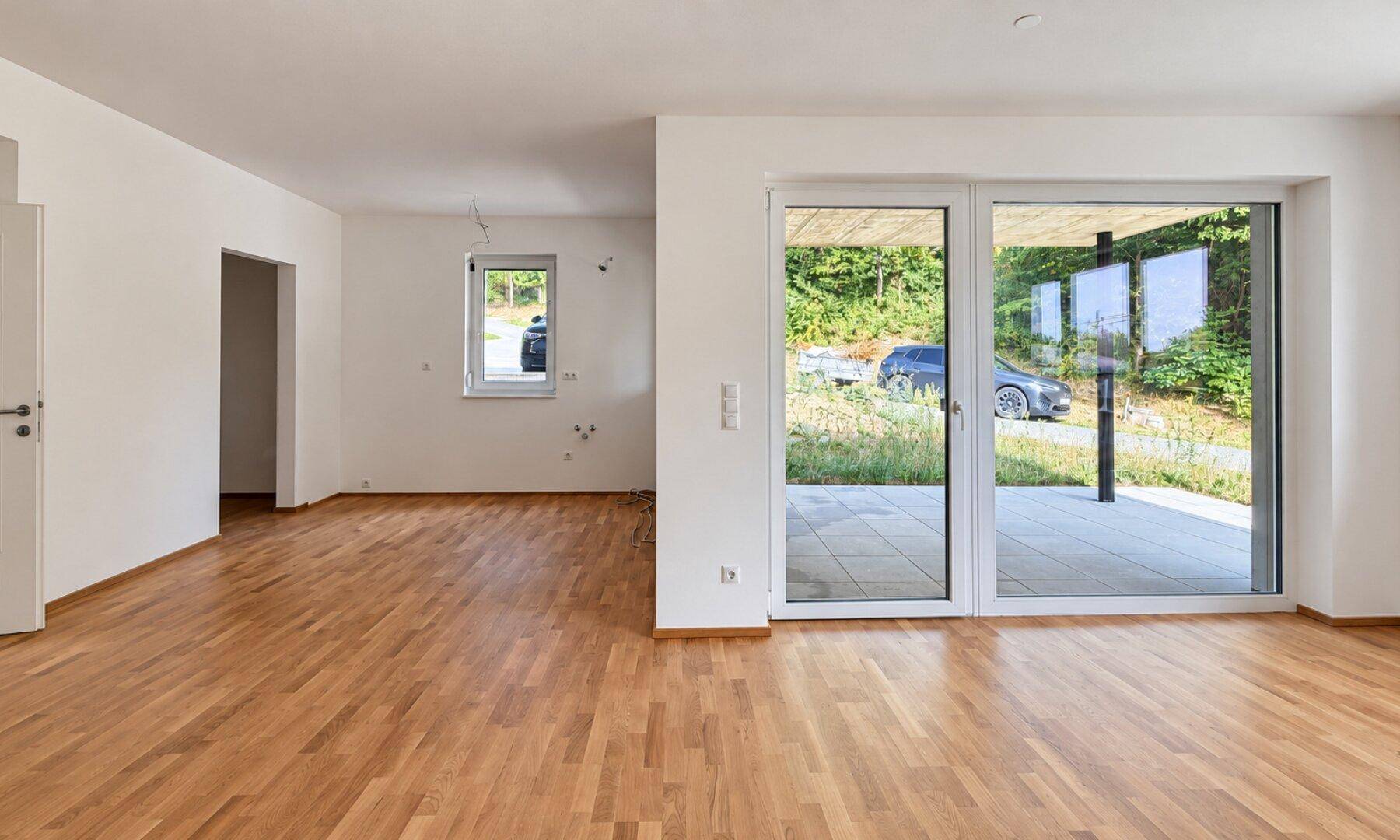 Geräumiges Wohnzimmer mit Holzboden, großen Schiebetüren und Blick auf den Außenbereich.