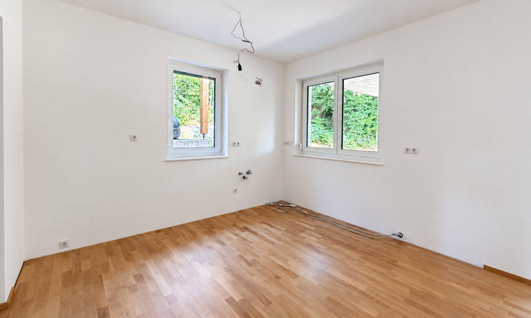 Leeres Schlafzimmer mit zwei Fenstern, Holzboden und viel natürlichem Licht.