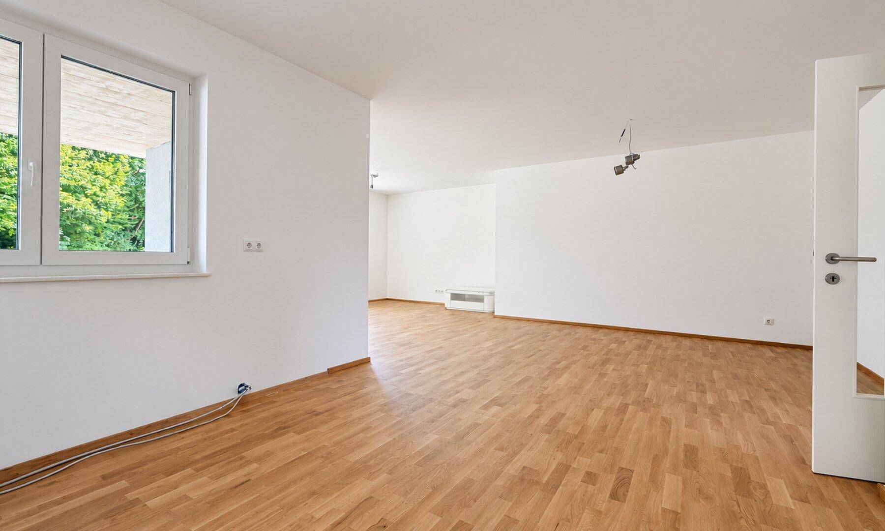 Heller Wohnbereich mit Holzboden und großem Fenster, bereit für individuelle Gestaltung.