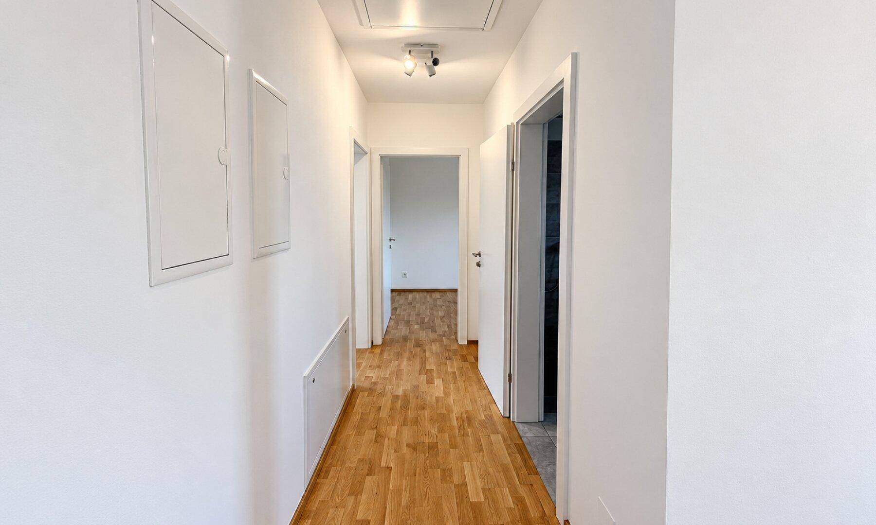 Langer Flur mit Holzboden, weißen Wänden und Zugang zu verschiedenen Räumen.