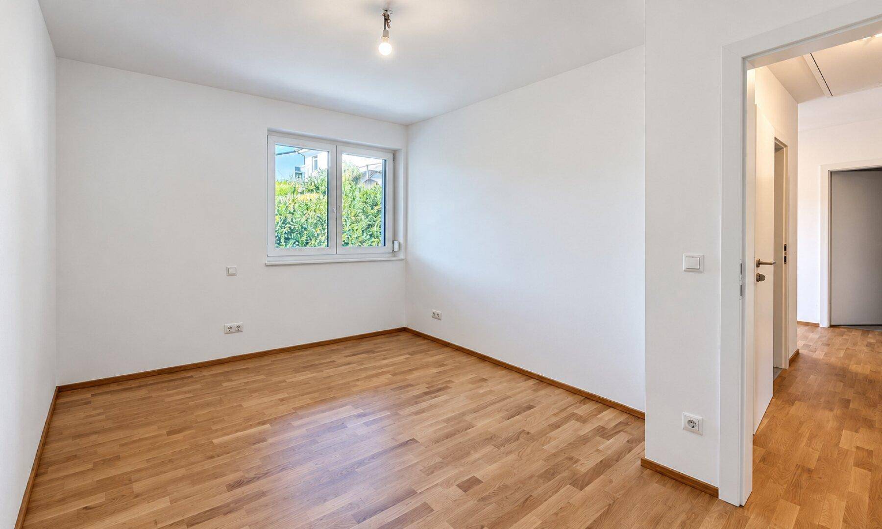 Helles Schlafzimmer mit Holzboden und Fenster, ideal als Kinder- oder Gästezimmer.