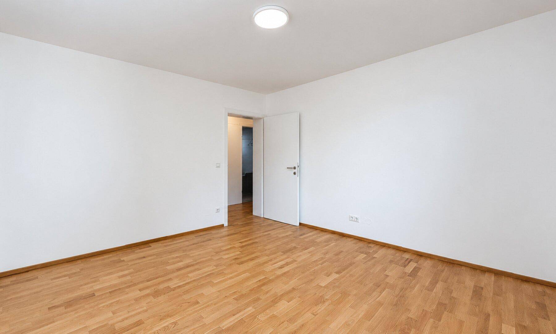 Modernes Schlafzimmer mit Holzboden und schlichter Deckenleuchte, bietet viel Platz.